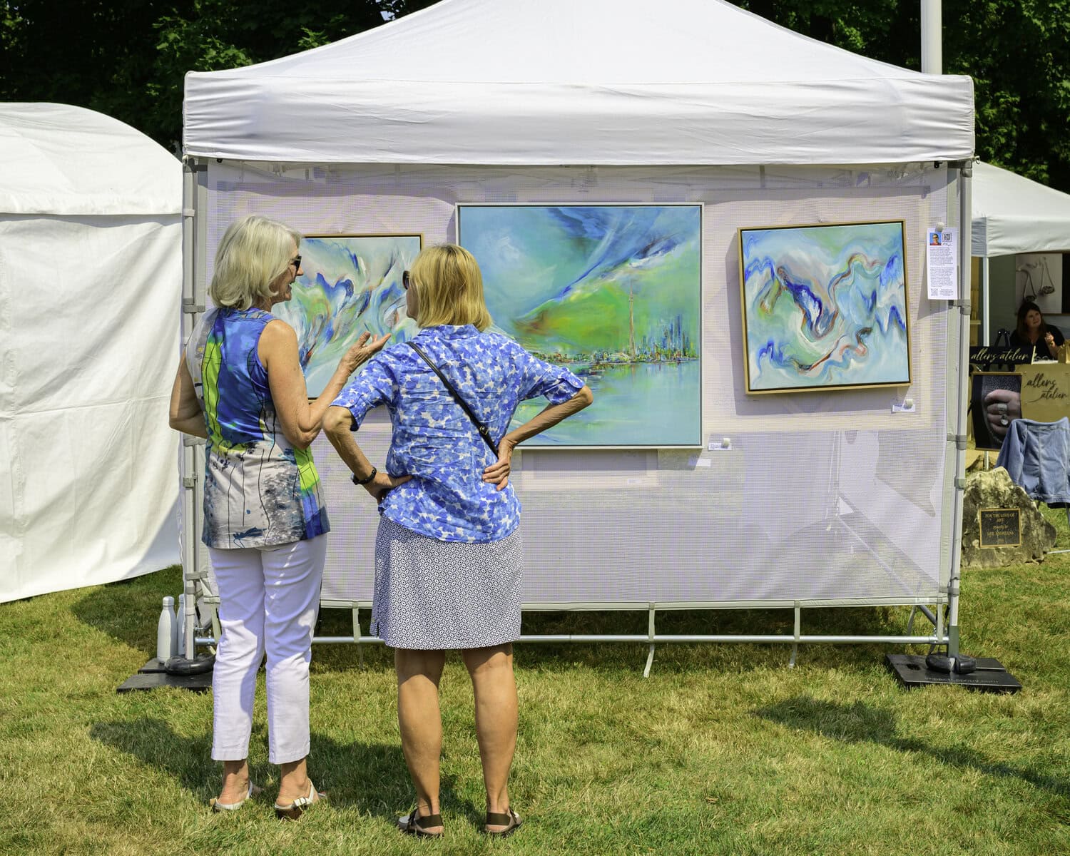 Two Art at the Pumphouse show-goers admire these impressionistic, water-inspired paintings, including the central piece depicting the Toronto city skyline.