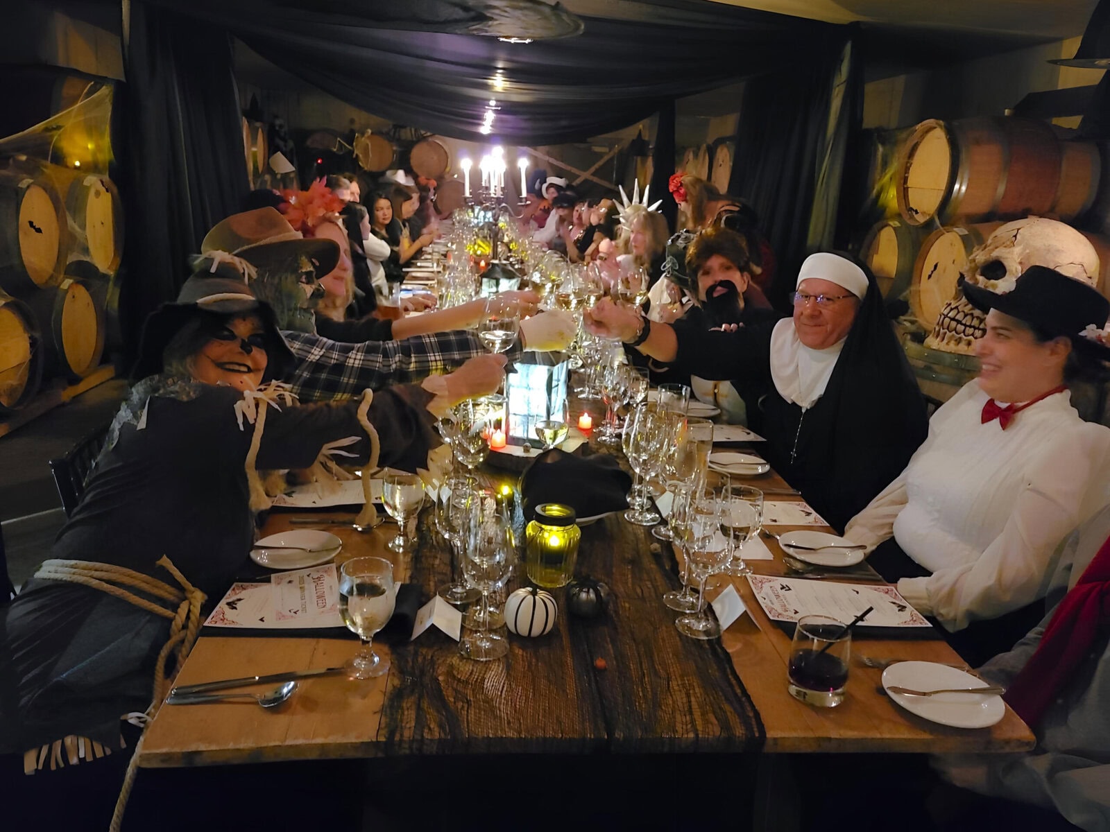 Guests in costume raise a toast inside the Ravine Vineyard barrel cellar during the Halloween gala dinner, surrounded by candlelight and oak casks. 