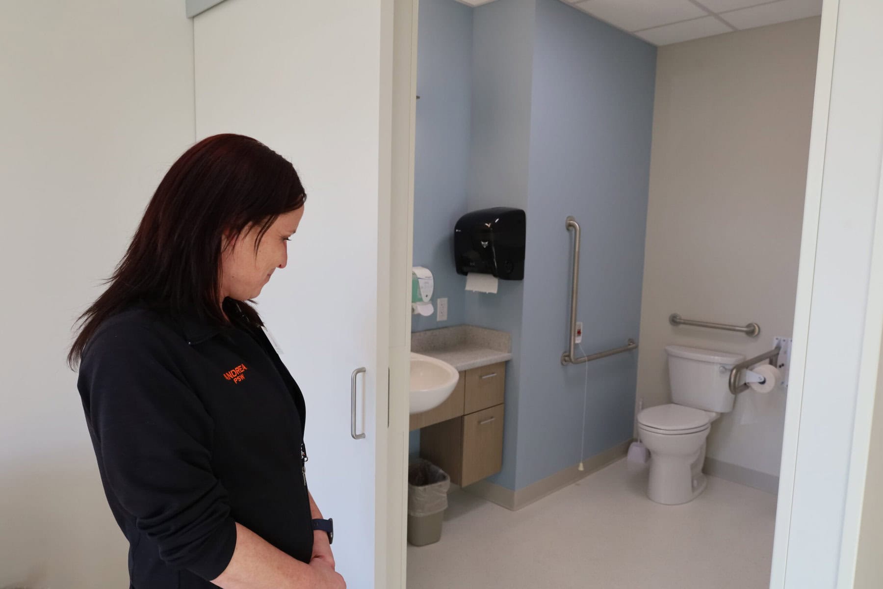 Personal support worker Andrea McQuay stands in the bathroom of a private room, highlighting its spacious and bright design at Pleasant Manor’s new long-term care home.