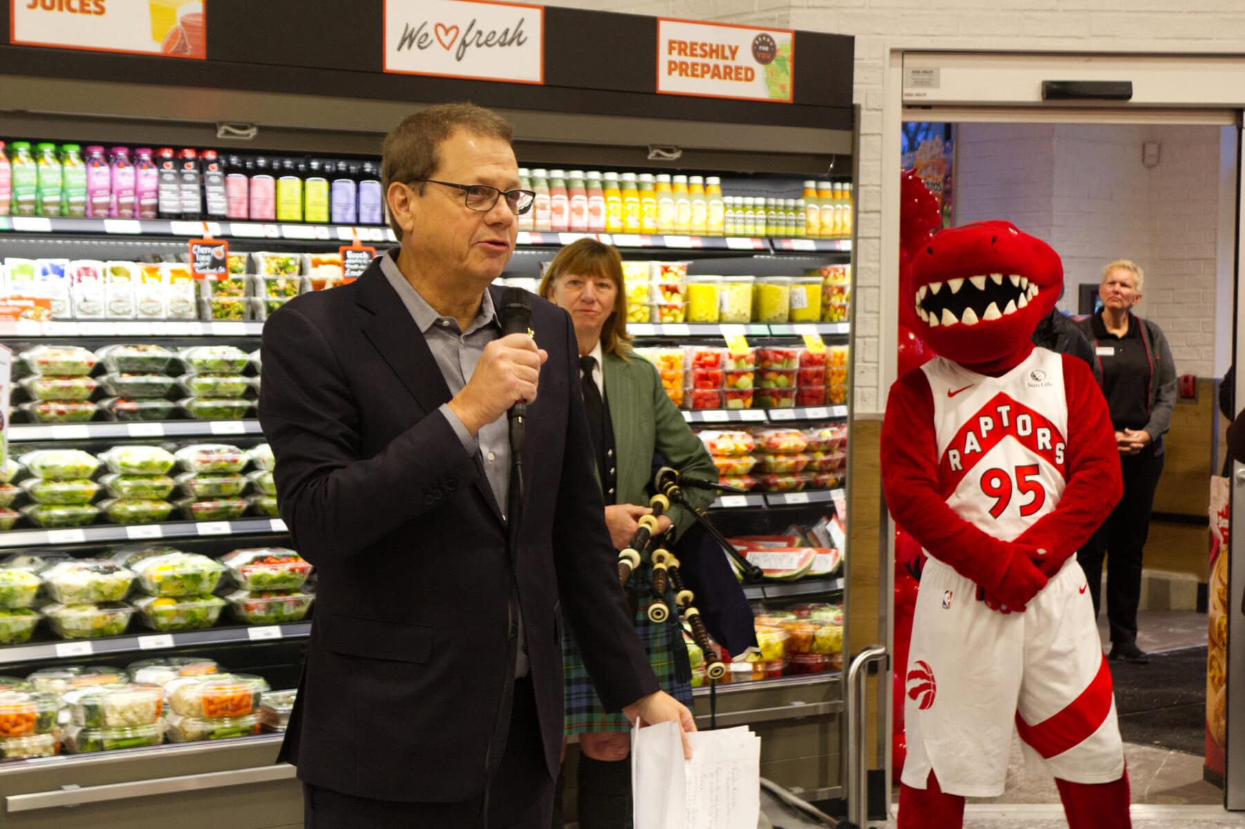 Former Sobeys CEO Michael Medline helped bring in Garrison Village's Foodland grocery store during their grand opening on Thursday, seen here speaking with bagpiper Kelly Buckley and the Toronto Raptors mascot.