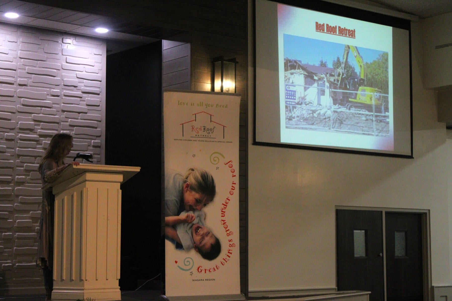 Red Roof Retreat founder and executive director Steffanie Bjorgan watches video of her former office being torn down and tells the crowd she “won’t miss it.” A new building is being built in its place.