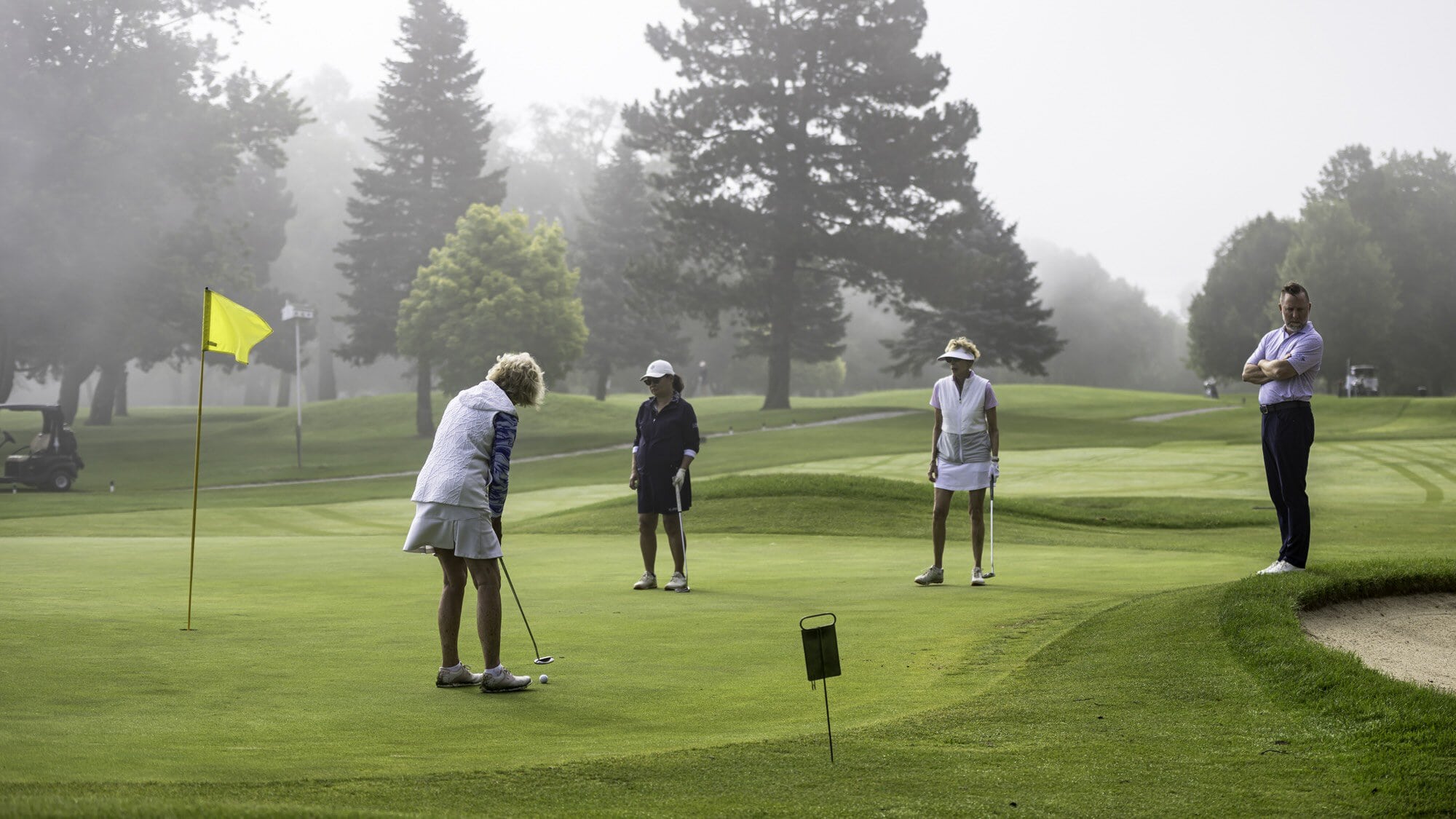 Martha Cruikshank putts on the fourth hole while playing partners May Chang and Sally Huck look on. At right is pro shop manager Darren Smith. 