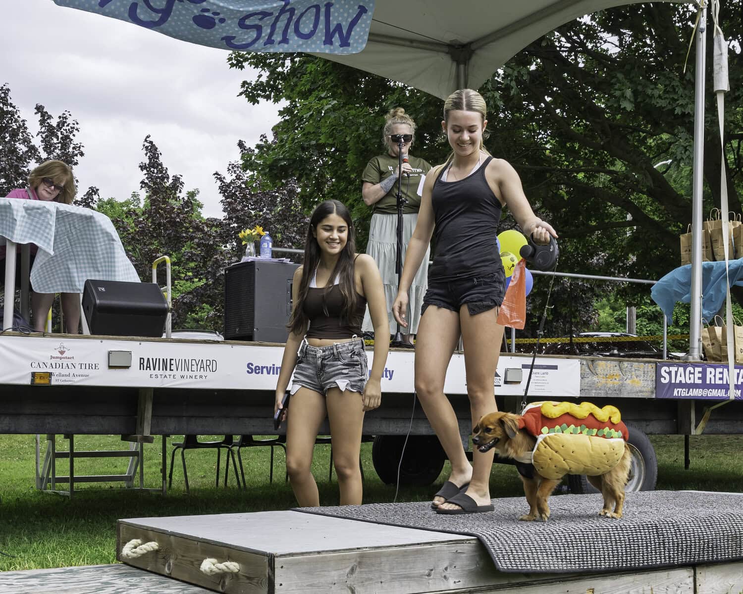 He's a "wiener"! Thirteen-year-olds Xenia Rigas and Capri Pratt present Tex the dog, wearing a sausage costume, at the dog show.