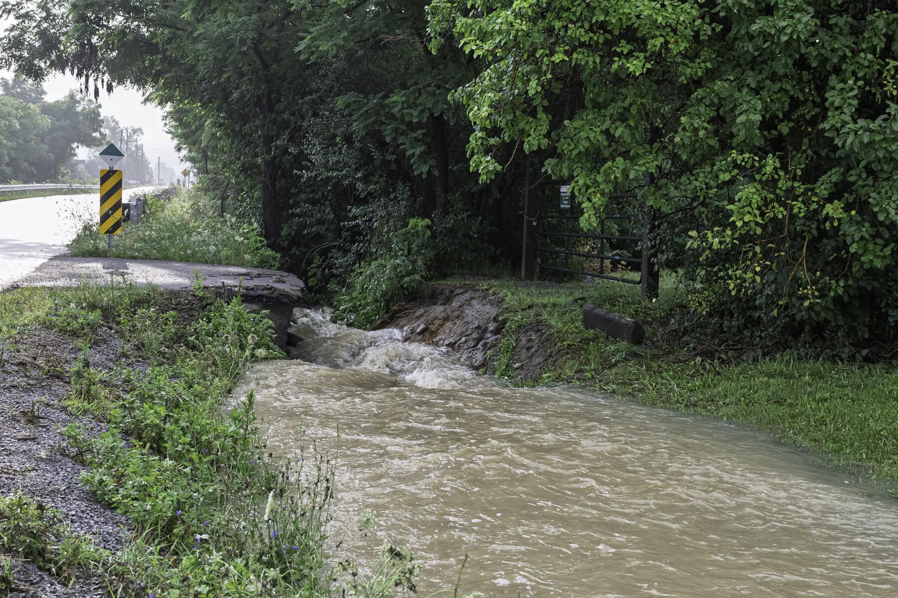 The entrance to the Line 3 Road reservoir culvert is washed out, with stormwater running rapidly through it.