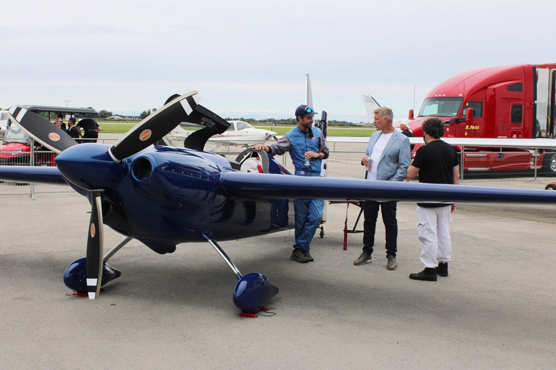An aerobatic pilot talks shop with guests beside his aircraft, one of several planes that shared the tarmac with the supercars.