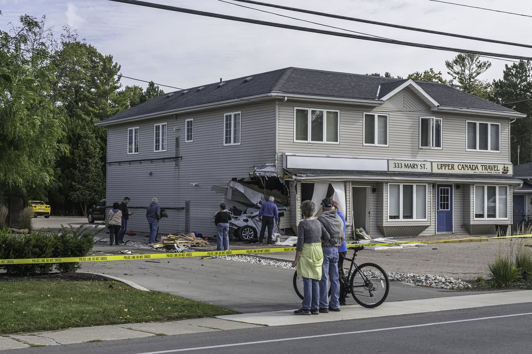 Onlookers observe the damage from the sidewalk on Mary Street. Part of the building’s exterior was torn open, a ground-floor window was damaged and debris was scattered around the property.