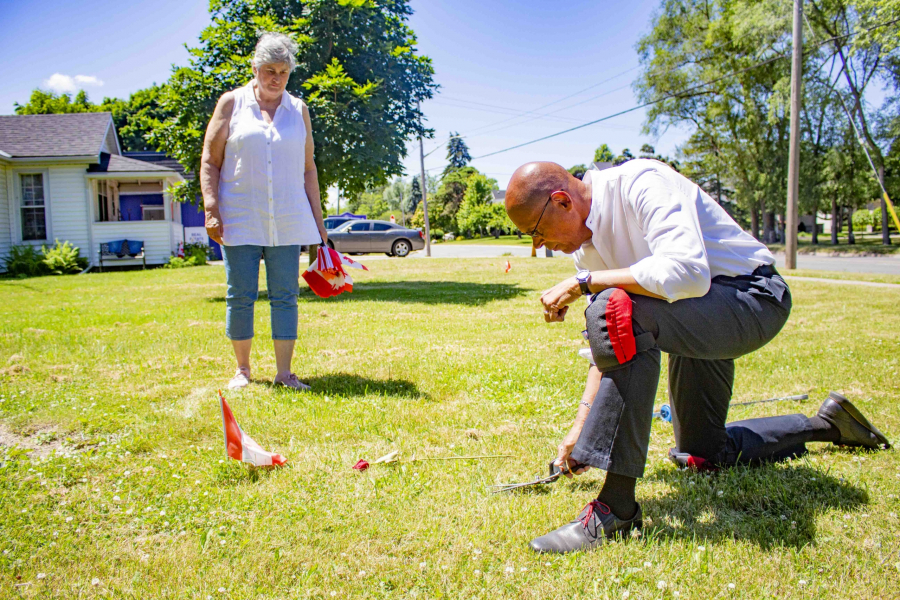 Jim Russell, dressed as always in business casual with knee pads, cuts the grass by hand around the Canadian flags he has installed at the Negro Burial Ground on Mississauga Street with his wife Marilyn Russell. An archaelogical company has submitted an assessment to dig up the buried headstones in the cemetery for $59,000.